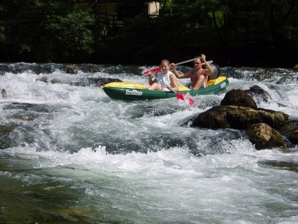 A river with rapids, a green and yellow raft with the word "helios" on it, and two people paddling.