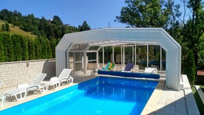 Una piscina con un deck de cristal, rodeada de sillas reclinables blancas.