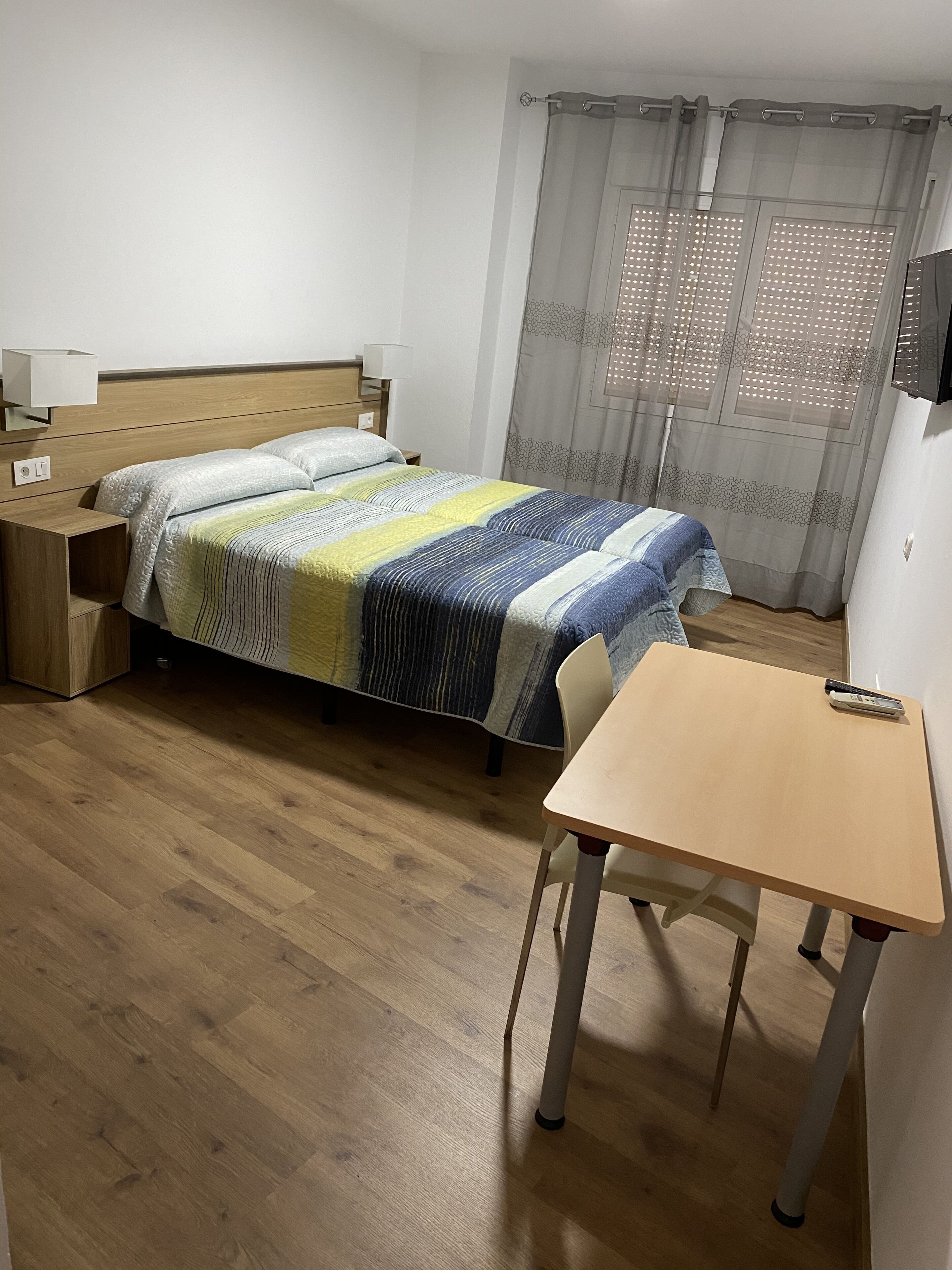 A bedroom with a bed, bedside table, lamp, and a desk with a chair.