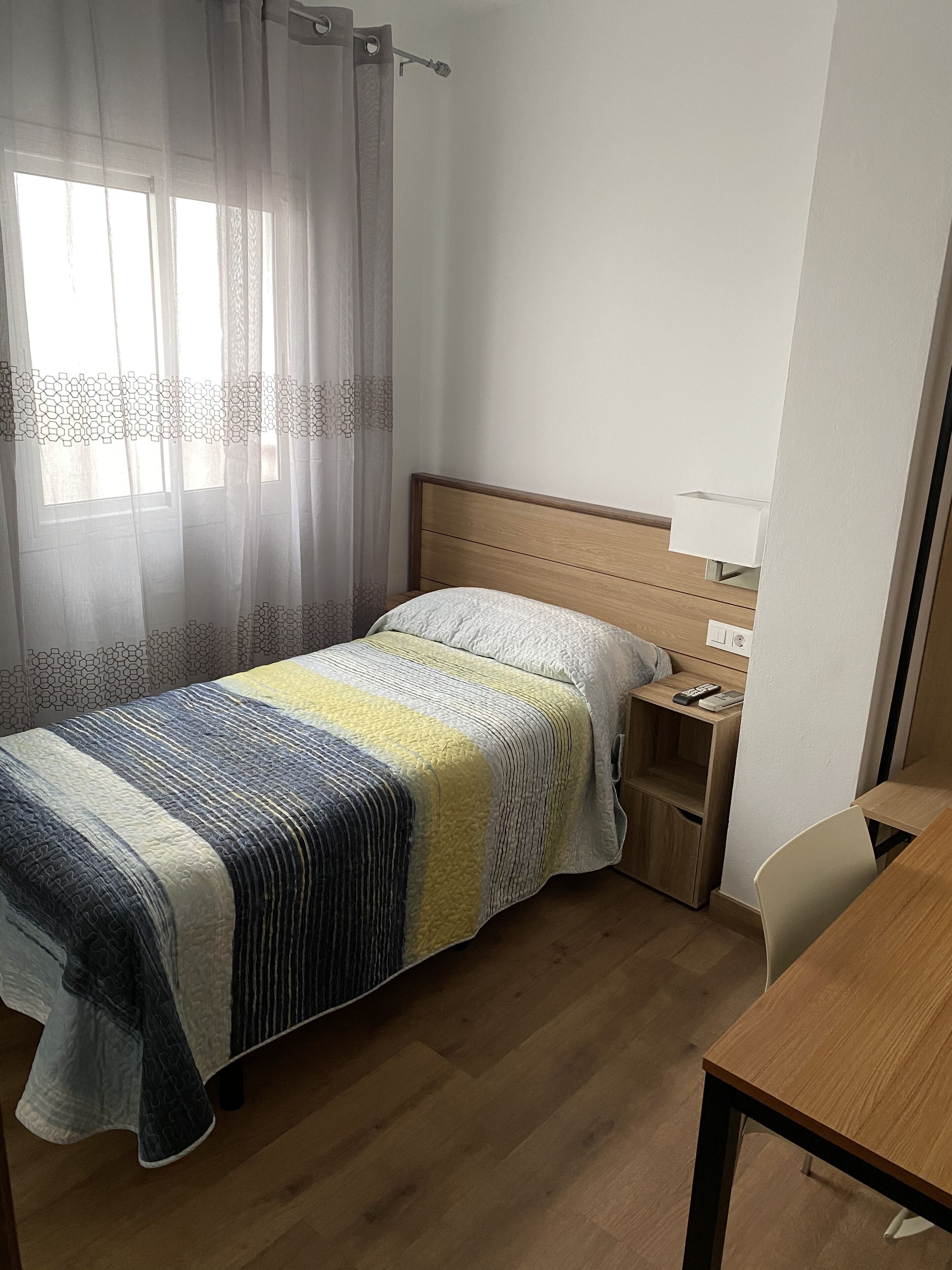 Un dormitorio con una cama de madera, una mesita de noche con una lámpara y una silla.