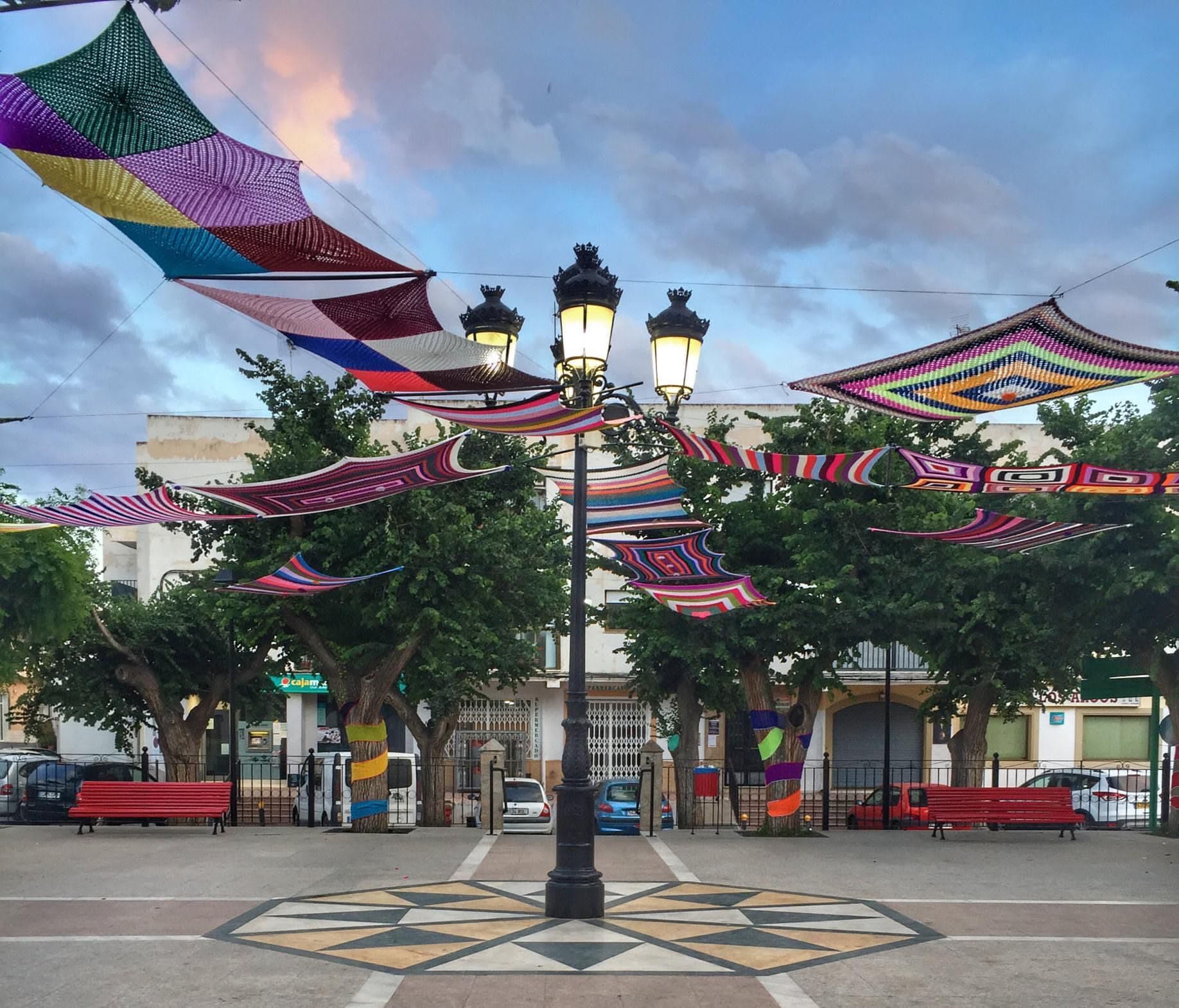 A public square with a patterned pavement, a street lamp, and colorful fabric decorations.