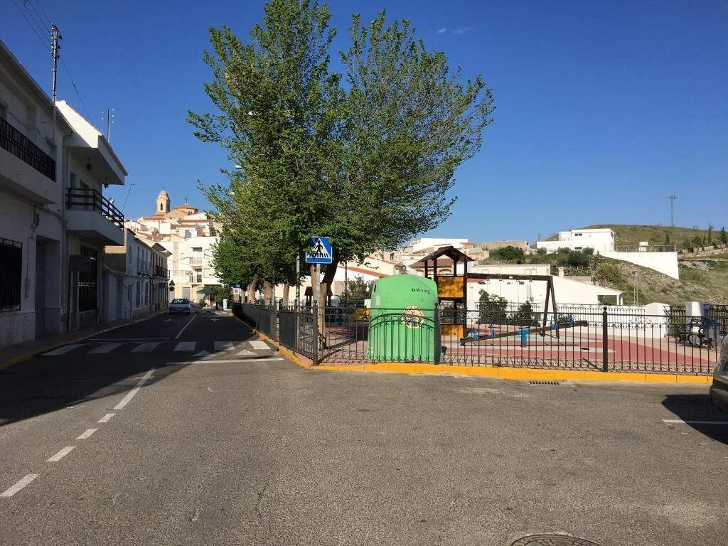 Una calle con edificios, una señal de paso para peatones, un bote de basura verde y una valla.