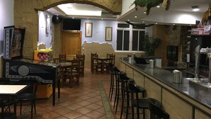 A restaurant with a stone archway, wooden tables and chairs, a bar area, and a television screen. - Hostal La Escapada (Uleila del Campo)