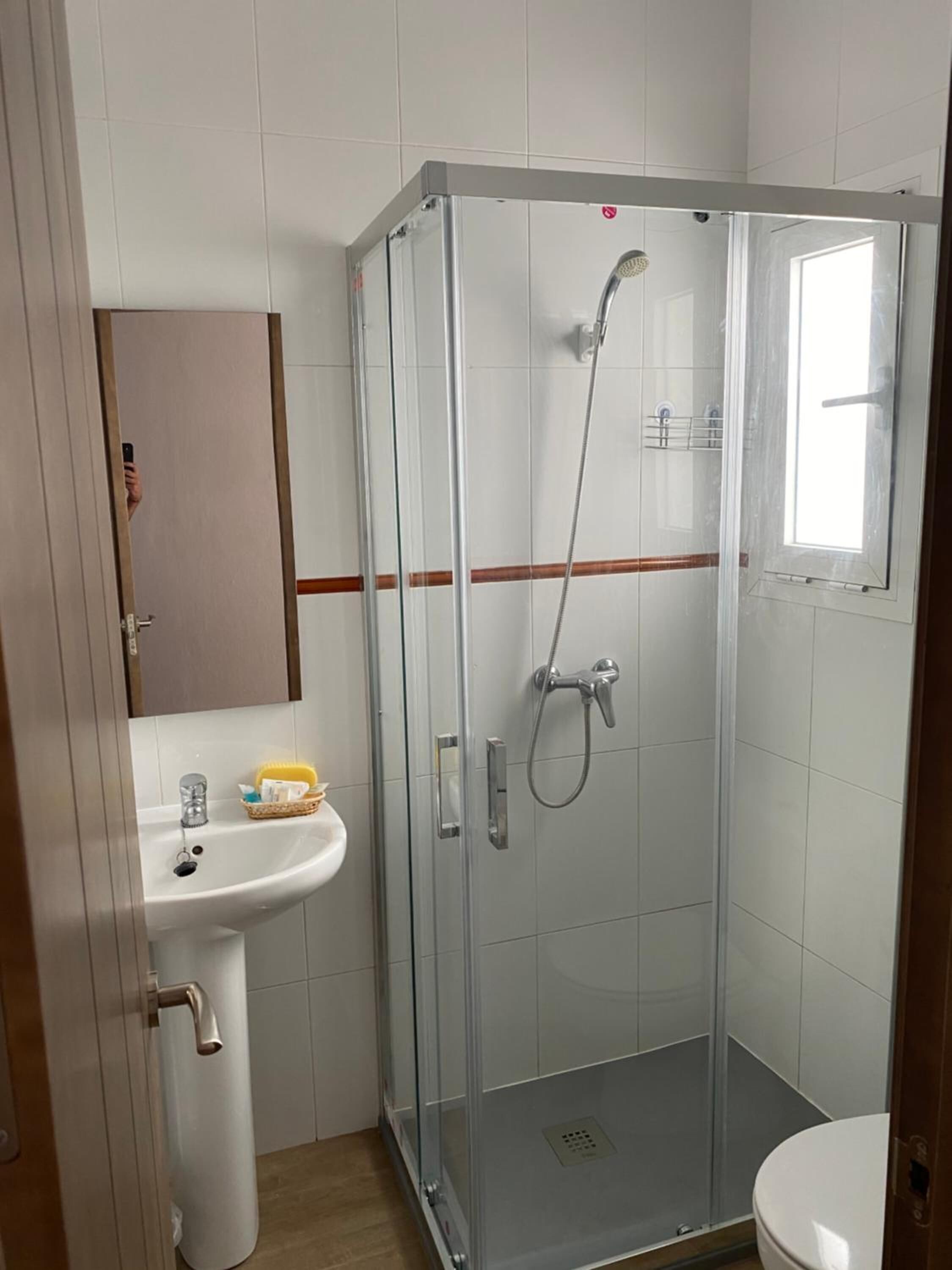 A small, modern bathroom with a glass-enclosed shower, a white sink, and a toilet.