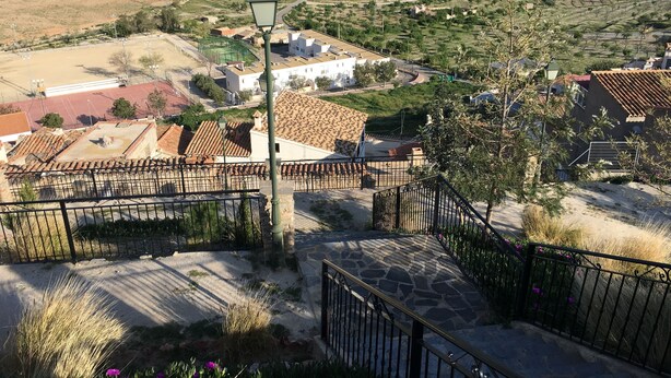 A town with terracotta-roofed buildings, a cobblestone pathway, and a street lamp. - Hostal La Escapada (Uleila del Campo)