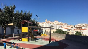 A playground with a seesaw, climbing structures, and a slide, set against a backdrop of residential buildings. - Hostal La Escapada (Uleila del Campo)