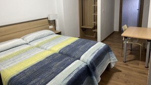 A bedroom with a bed, bedside table, lamp, wooden wardrobe, and a small table with chairs. - Hostal La Escapada (Uleila del Campo)