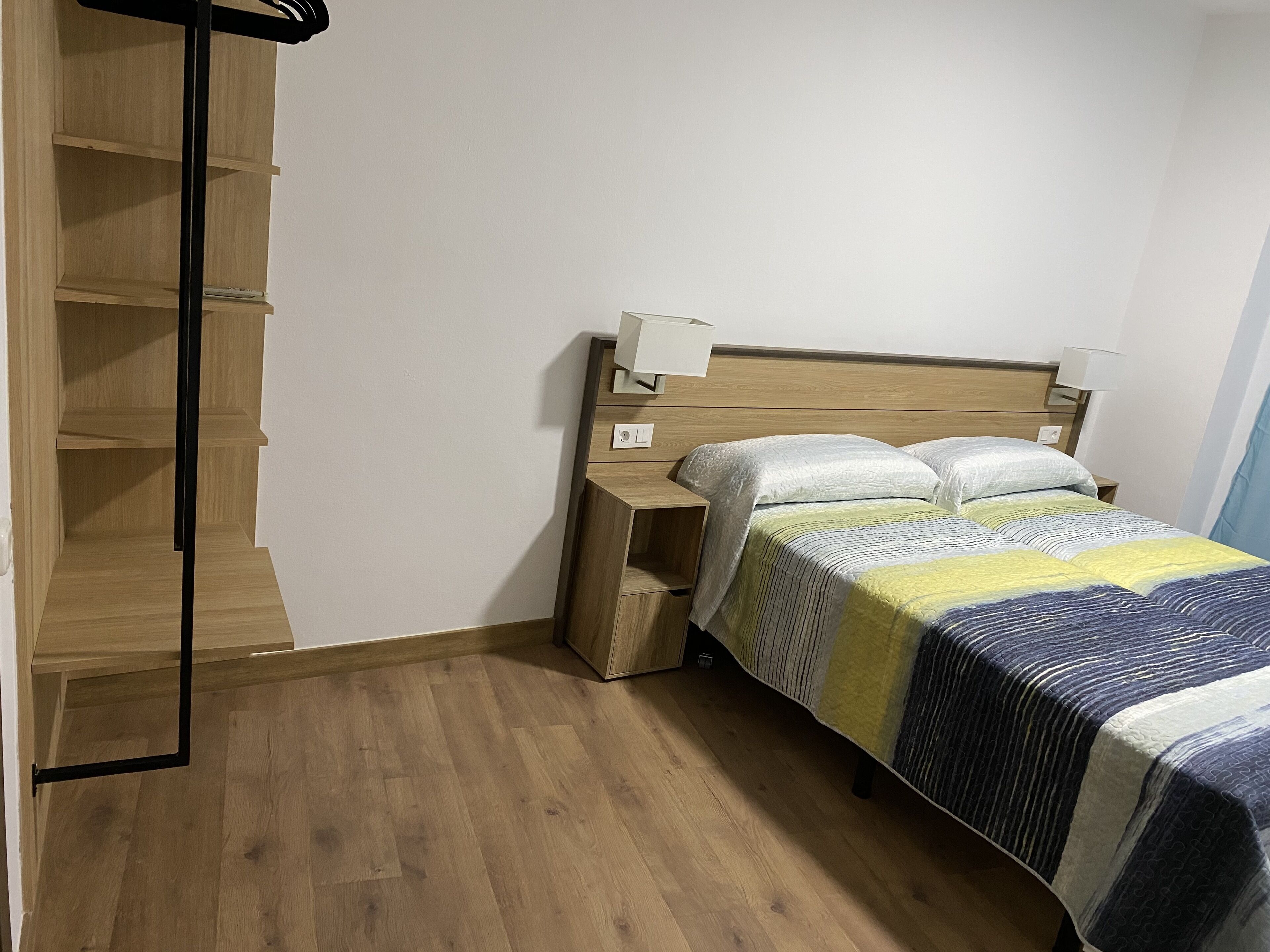 Une chambre avec un plancher en bois, un lit recouvert d’une courtepointe à rayures, deux lampes de chevet et une table de chevet.