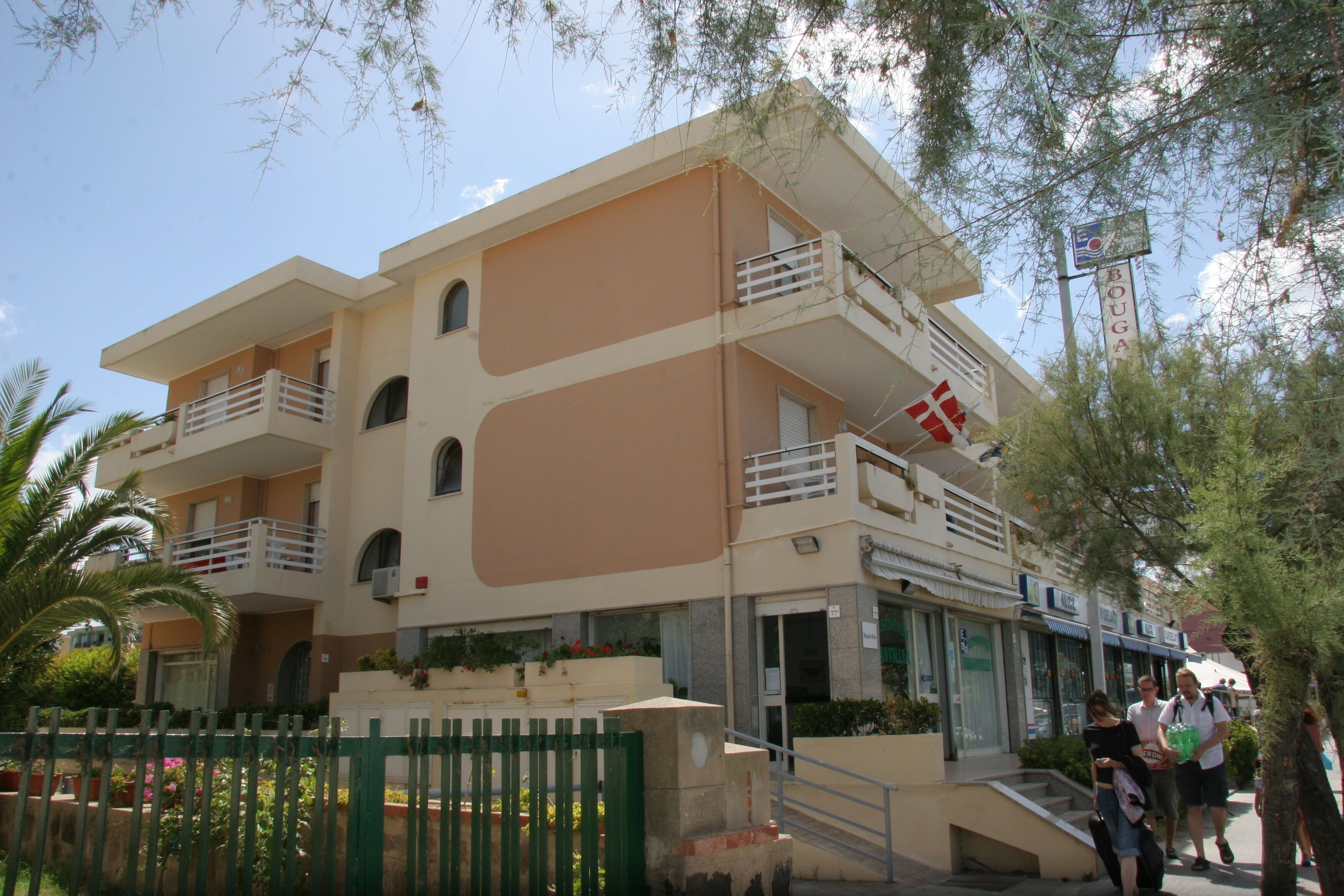 A multi-story building with balconies, a staircase, and a green fence.