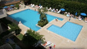 A large outdoor swimming pool with multiple sections, surrounded by lounge chairs and umbrellas.