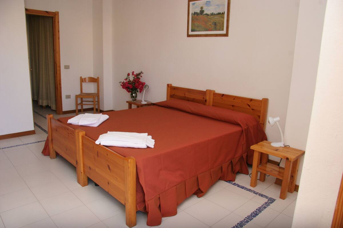 A bedroom with a wooden bed, a chair, a nightstand, and a painting on the wall.