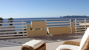 A balcony with wicker furniture, a view of the sea, and a white railing.