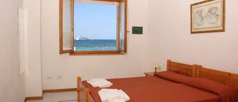 A bedroom with a large bed, a window with a view of the sea and a ship, and a framed map on the wall.