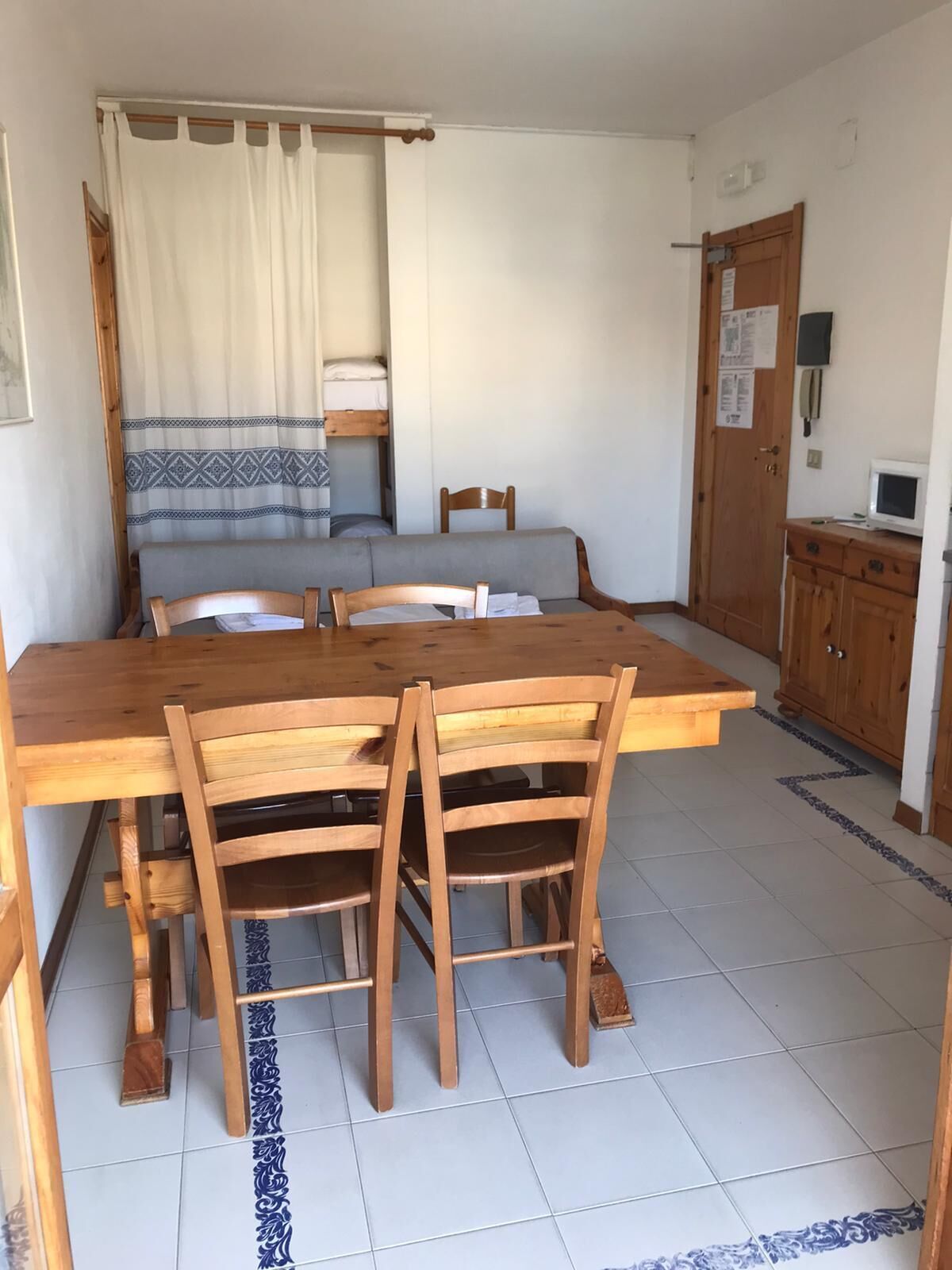 Una stanza compatta con un tavolo e sedie in legno, un letto a castello, un angolo cottura piccolo e una porta con un avviso.