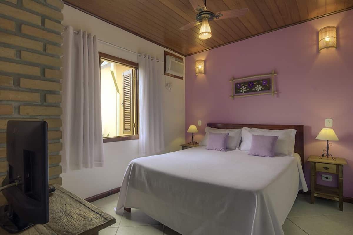 A bedroom with a bed, two bedside lamps, a TV, and a window with curtains.