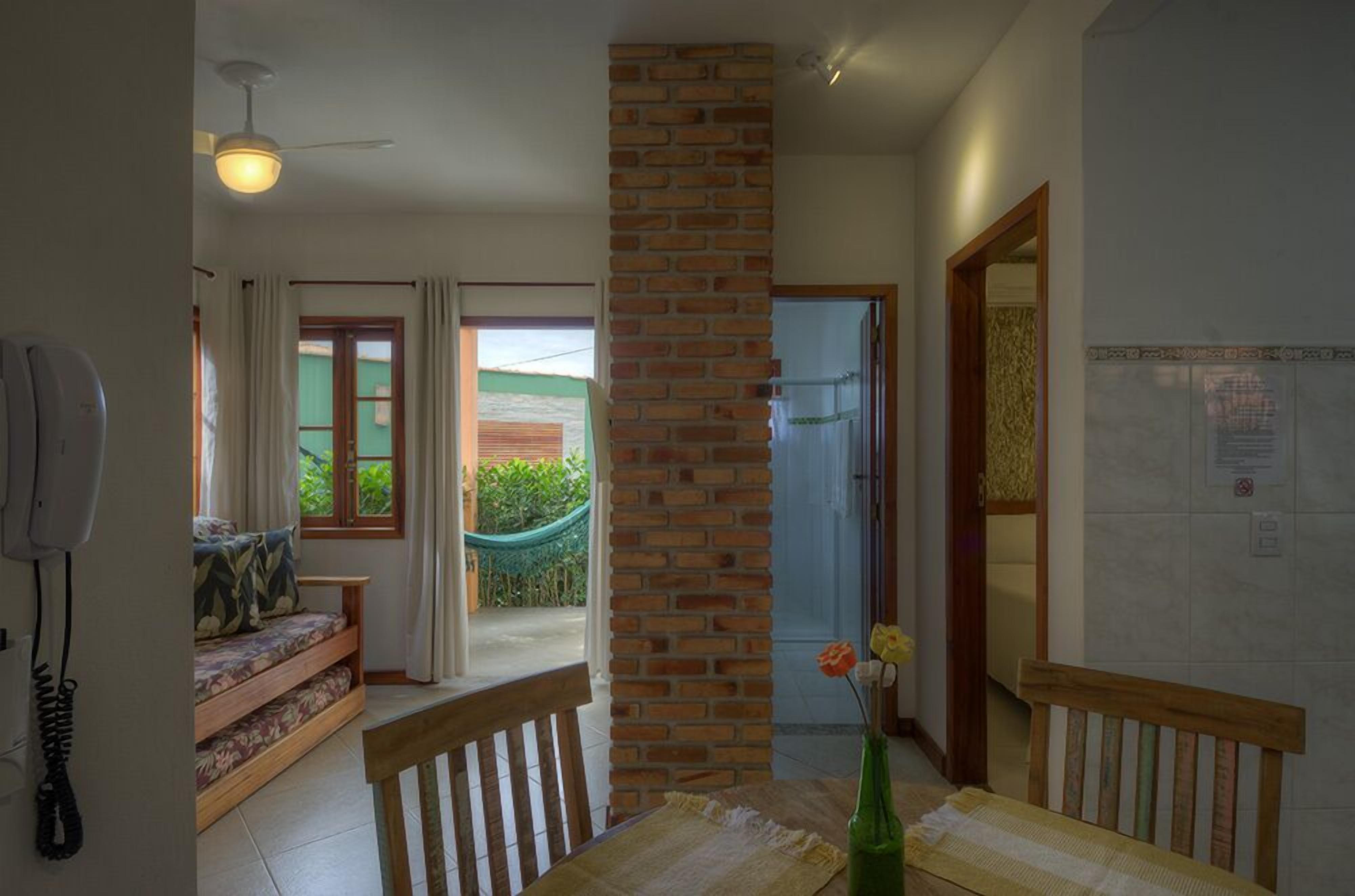 A room with a brick column, a dining table with chairs, a sofa with cushions, a telephone, and a view of a green outdoor area.