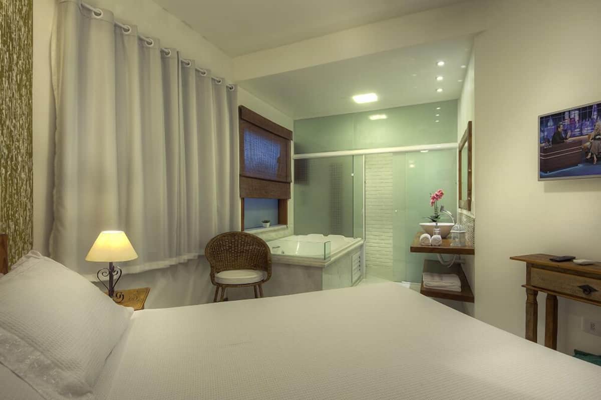 A hotel room with a bed, a chair, a desk, a bathroom with a bathtub, and a shower.