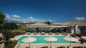 A rooftop pool area with lounge chairs and umbrellas, overlooking a mountainous landscape.