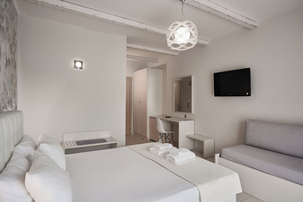 Una habitación de hotel moderna con cama, escritorio, sofá, televisión y baño a la vista.