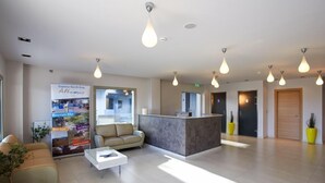A modern lobby with a reception desk, seating area, and a large poster advertising local attractions. - Altamar Hotel (Istiaia-Aidipsos)