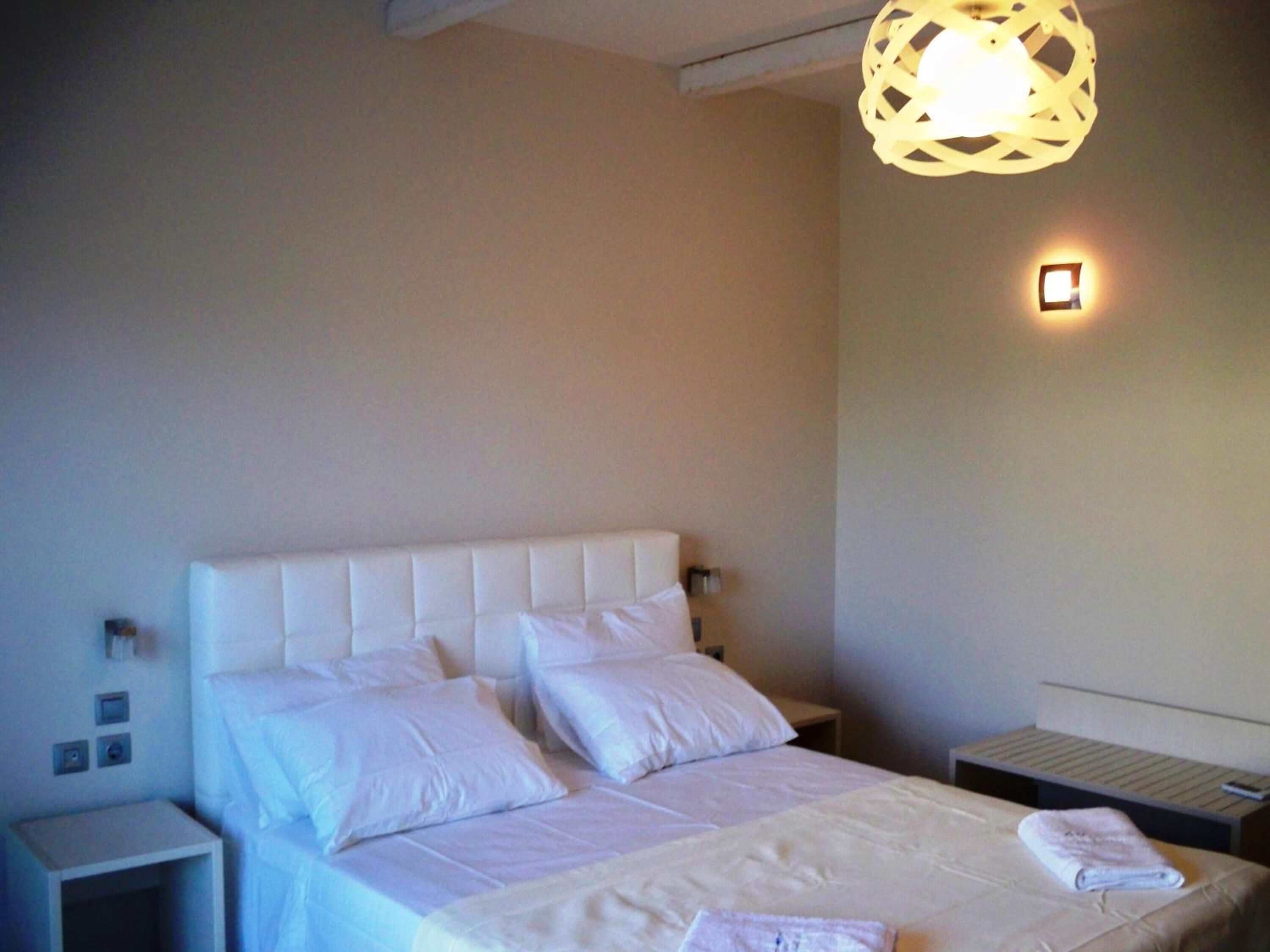 A neatly made bed with white linens, a bedside table, a wall-mounted light, and a small bedside table with a remote control.