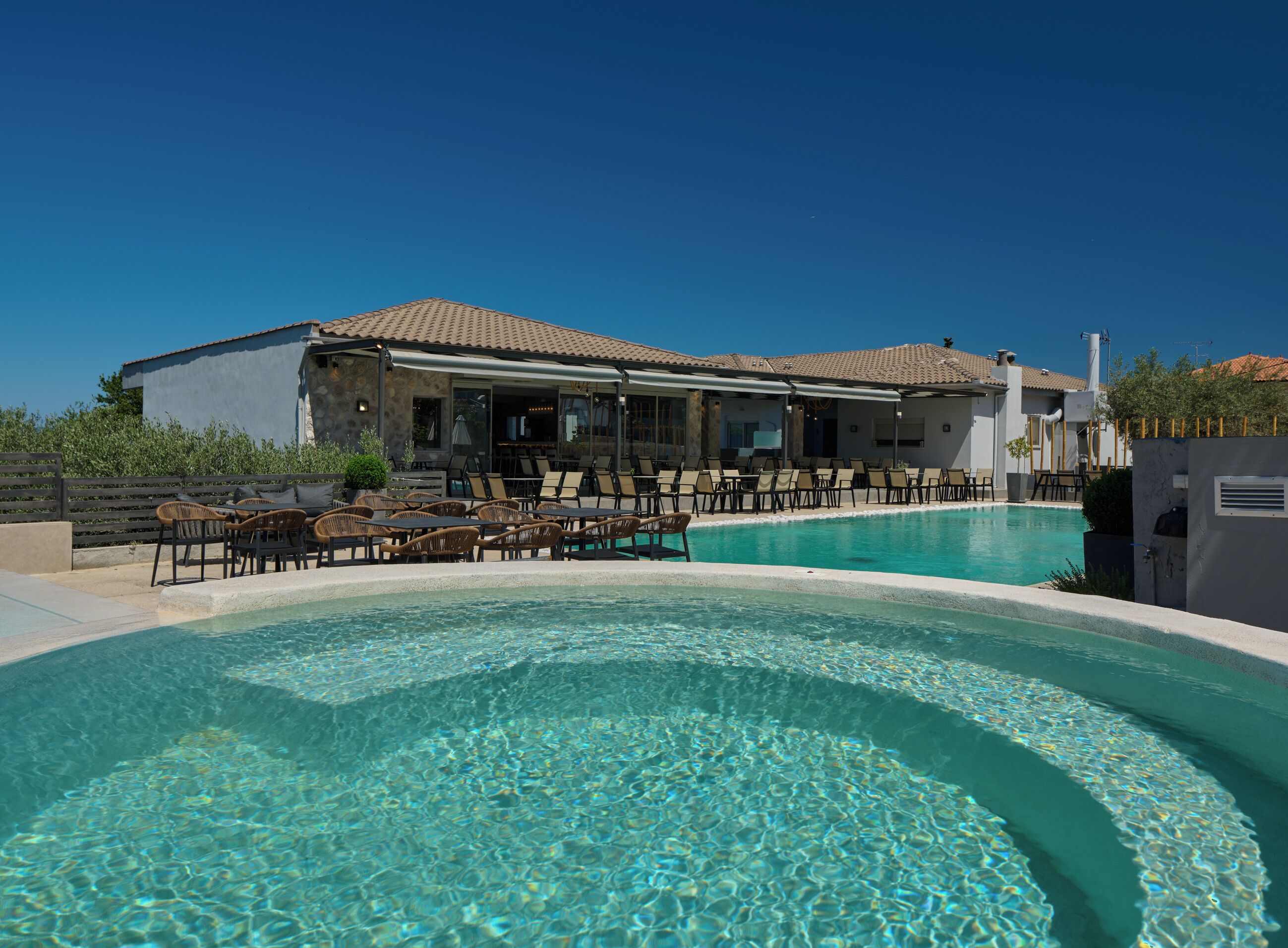 Un área junto a la piscina con sillones de descanso y un edificio con tejado de azulejos.