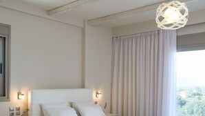 A modern bedroom with a large bed, bedside lamps, a view of the outdoors, and a hanging light fixture. - Altamar Hotel (Istiaia-Aidipsos)