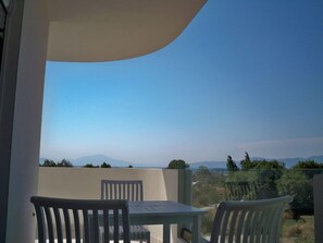 A balcony with two white chairs and a table, overlooking a mountainous landscape.