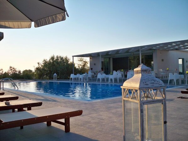 A pool area with lounge chairs, a covered seating area, and a glass-enclosed structure.