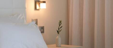 A hotel room with a bed, a bedside table with a lamp, and a vase with a plant.