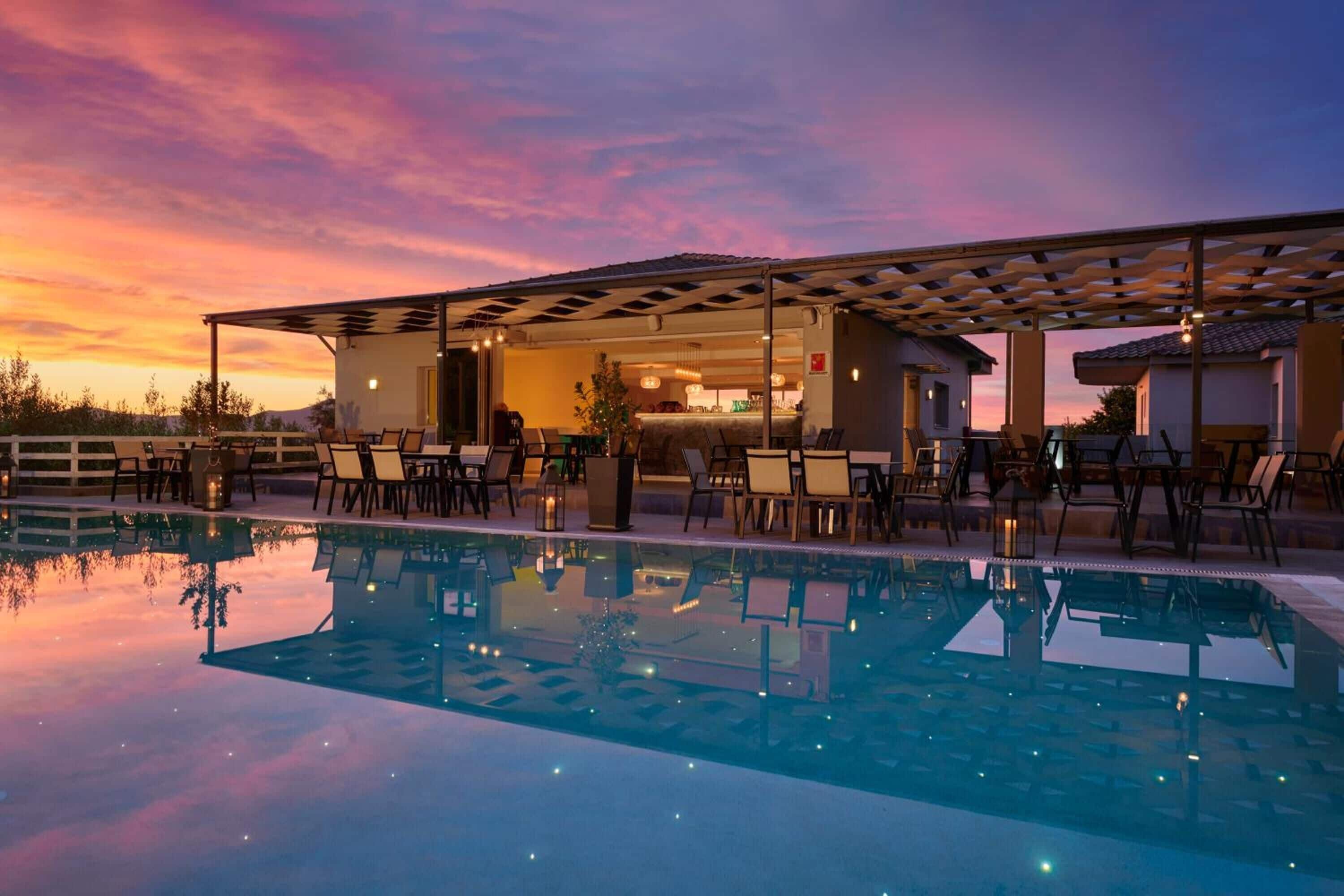 A poolside area with a covered seating area and a pool reflecting the sunset.