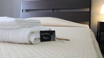 Un letto rifatto con cura, un asciugamano bianco piegato e un cartello nero che recita "Guest House Minas".