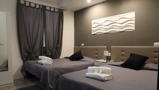 Habitación de hotel con dos camas, un ventanal con cortinas, un aplique en la pared y una mesita de noche con lámpara.