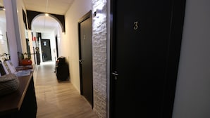 Un pasillo con suelo de madera, una puerta negra con el número 3 y una pared con textura.