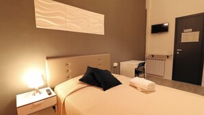 Una habitación de hotel con cama, mesita de noche con lámpara, una silla, televisor y puerta con letrero.
