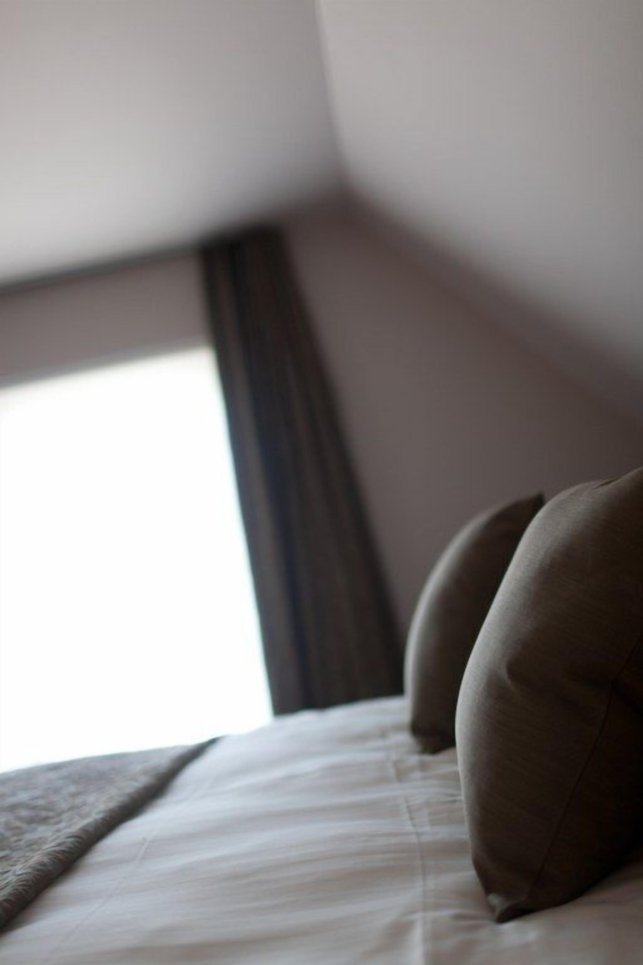 Una cama con colchón blanco y dos almohadas, una ventana con vista a un edificio y una cortina oscura.
