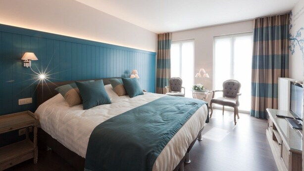 A modern hotel room with a large bed, two chairs, a TV, and a desk. - B&B Riche Terre (Damme)