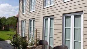 A two-story house with a patio area featuring a round table and two chairs. - B&B Riche Terre (Damme)