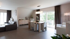 A modern living room with a sofa, a dining table, and a kitchen area. - B&B Riche Terre (Damme)