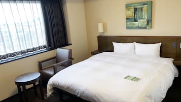 A hotel room with a large bed, a desk, a chair, a window with curtains, a painting on the wall, and a nightstand with a lamp.