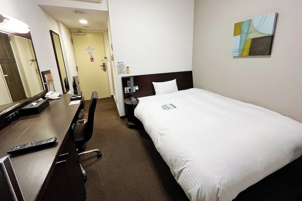 A hotel room with a bed, a desk, a chair, a telephone, and a painting on the wall.