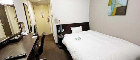 A hotel room with a bed, a desk, a chair, a telephone, and a painting on the wall.