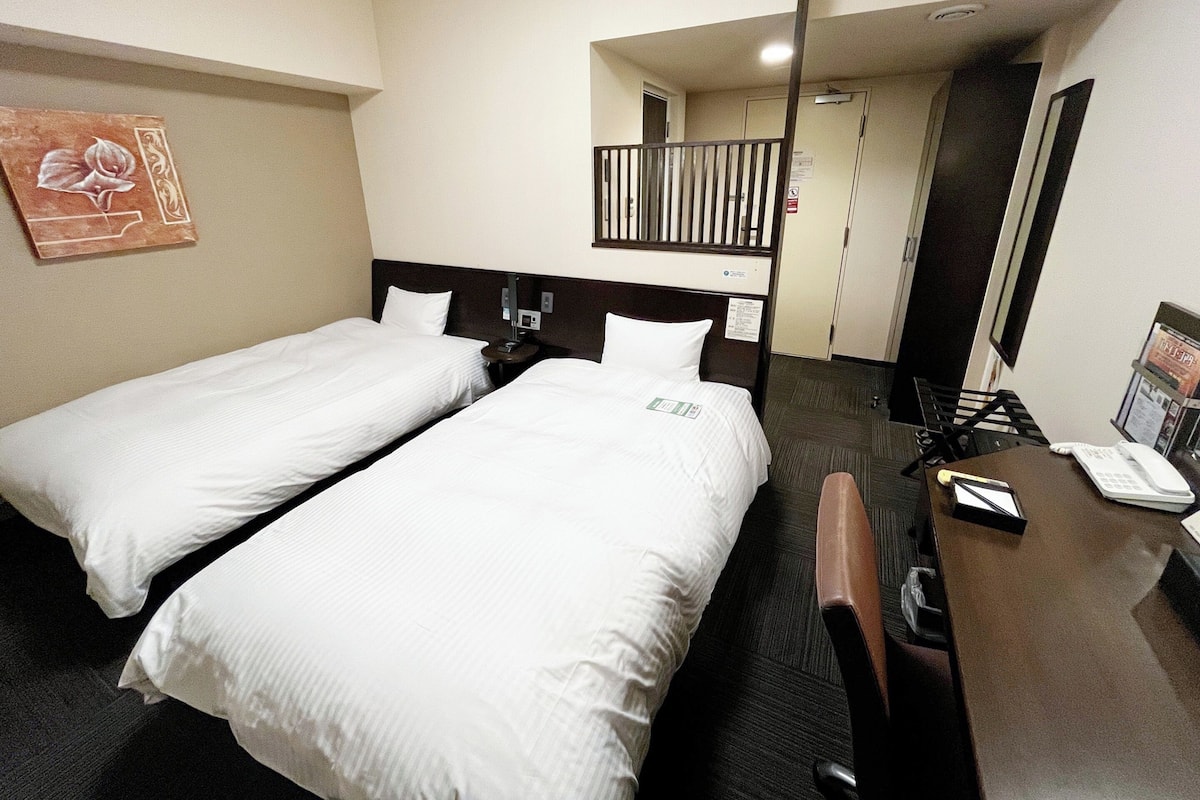 A hotel room with two single beds, a desk with a telephone, and a mirror.