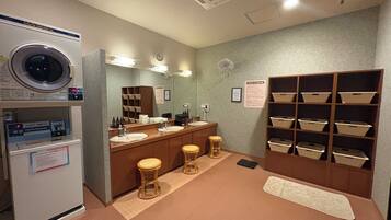 A hotel bathroom with a washing machine, sinks, a mirror, and storage baskets.
