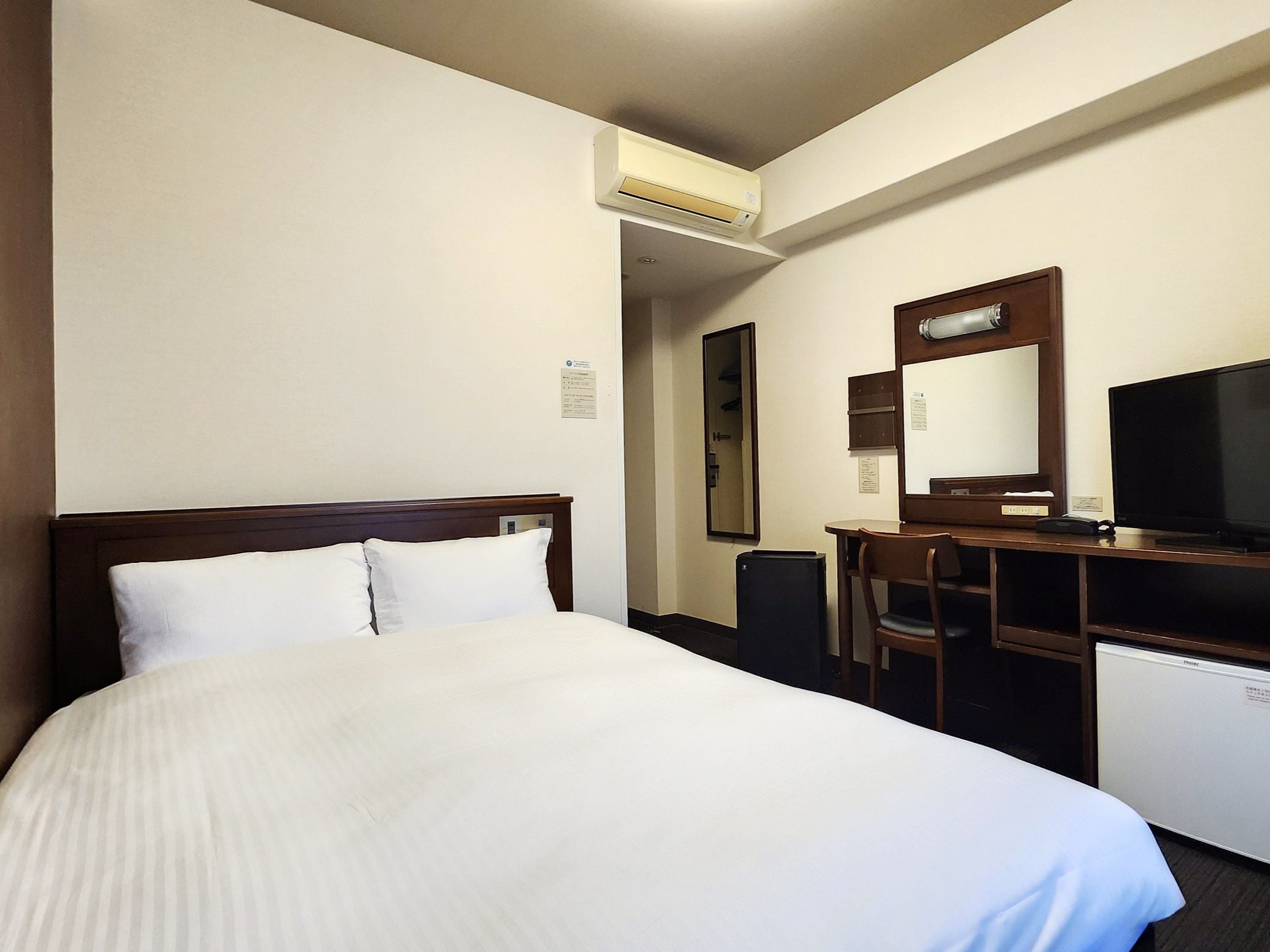 A hotel room with a bed, a desk, a television, and an air conditioning unit.