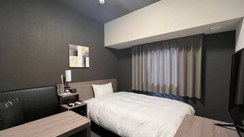 A hotel room with a bed, a desk, a chair, a nightstand, a lamp, a clock, and a window with curtains.