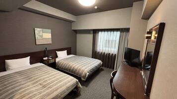 Habitación de hotel con dos camas, un escritorio, un televisor y una ventana con cortinas.