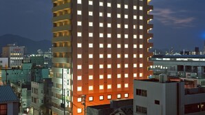 A tall hotel with a green neon sign at the top, multiple floors, and a modern architectural design. - Hotel Route Inn Tokuyama Ekimae (Shunan)