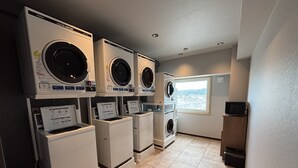A laundry facility with multiple washing machines and dryers, a window with a view, and a tiled floor. - Hotel Route Inn Tokuyama Ekimae (Shunan)