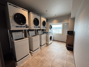 A laundry facility with multiple washing machines and dryers, a window with a view, and a tiled floor. - Hotel Route Inn Tokuyama Ekimae (Shunan)